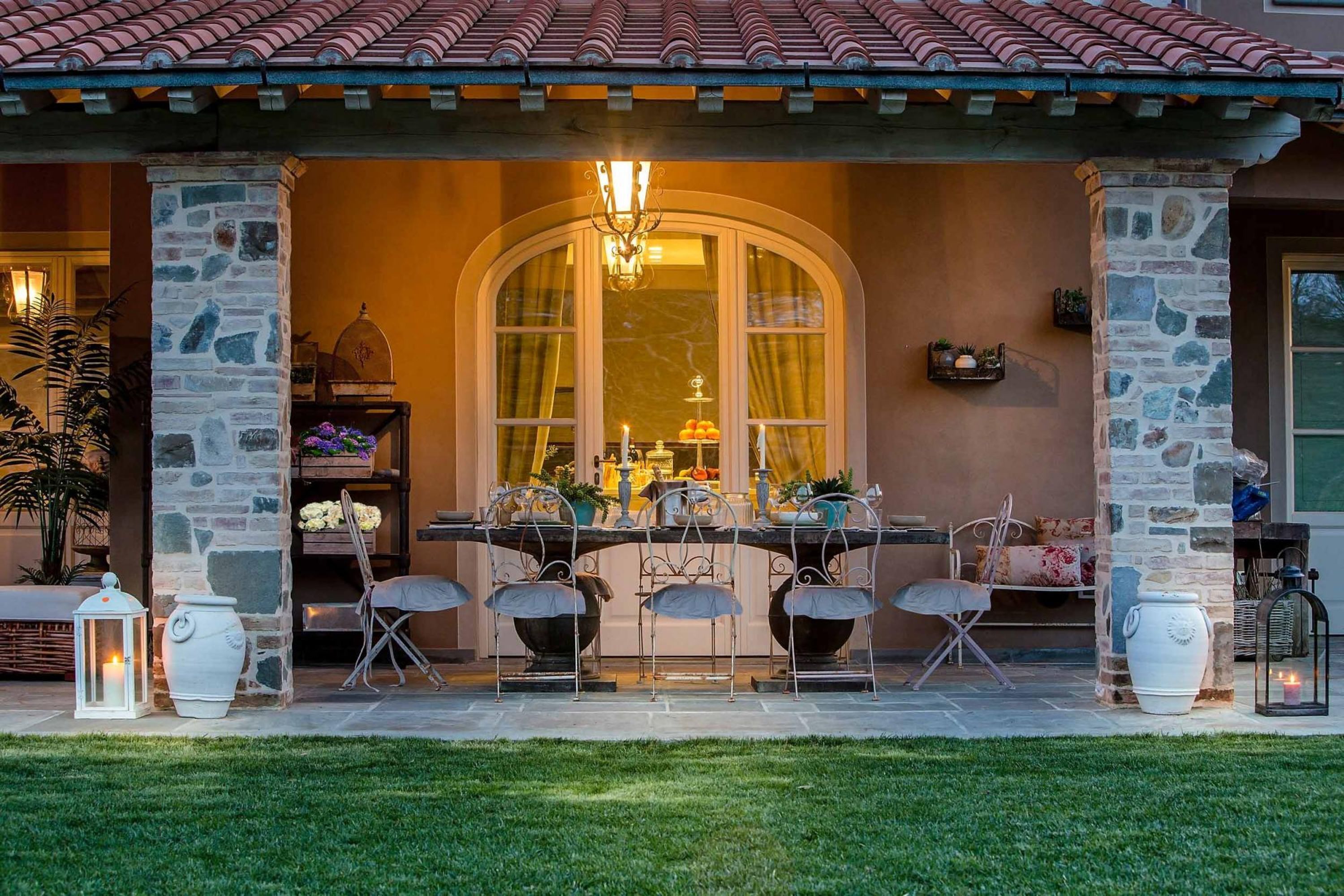 Una casa de piedra con un porche cubierto, una mesa de comedor con sillas y un gran ventanal.