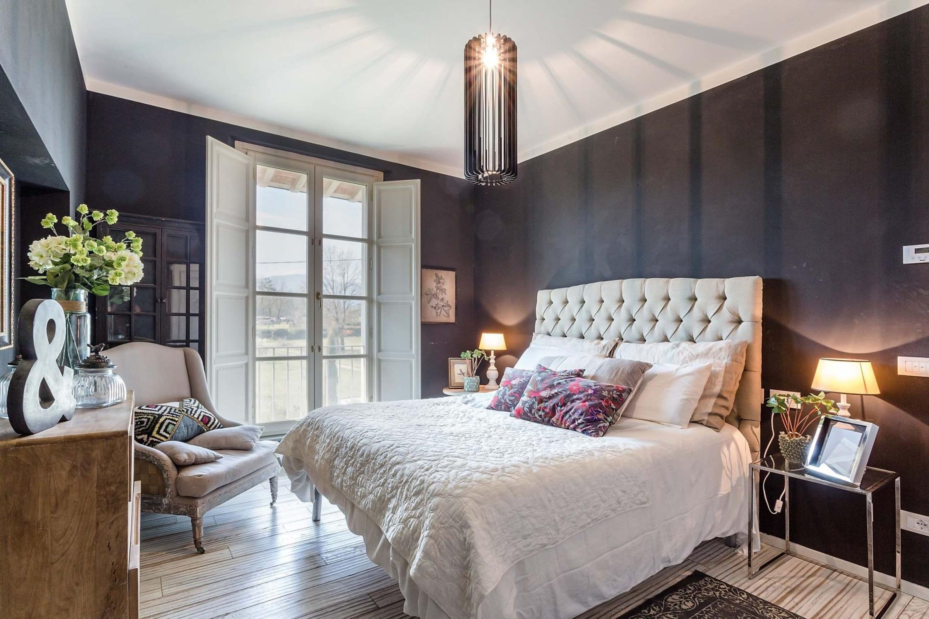 A bedroom with a large bed, a chair, a bedside table, and a hanging light fixture.
