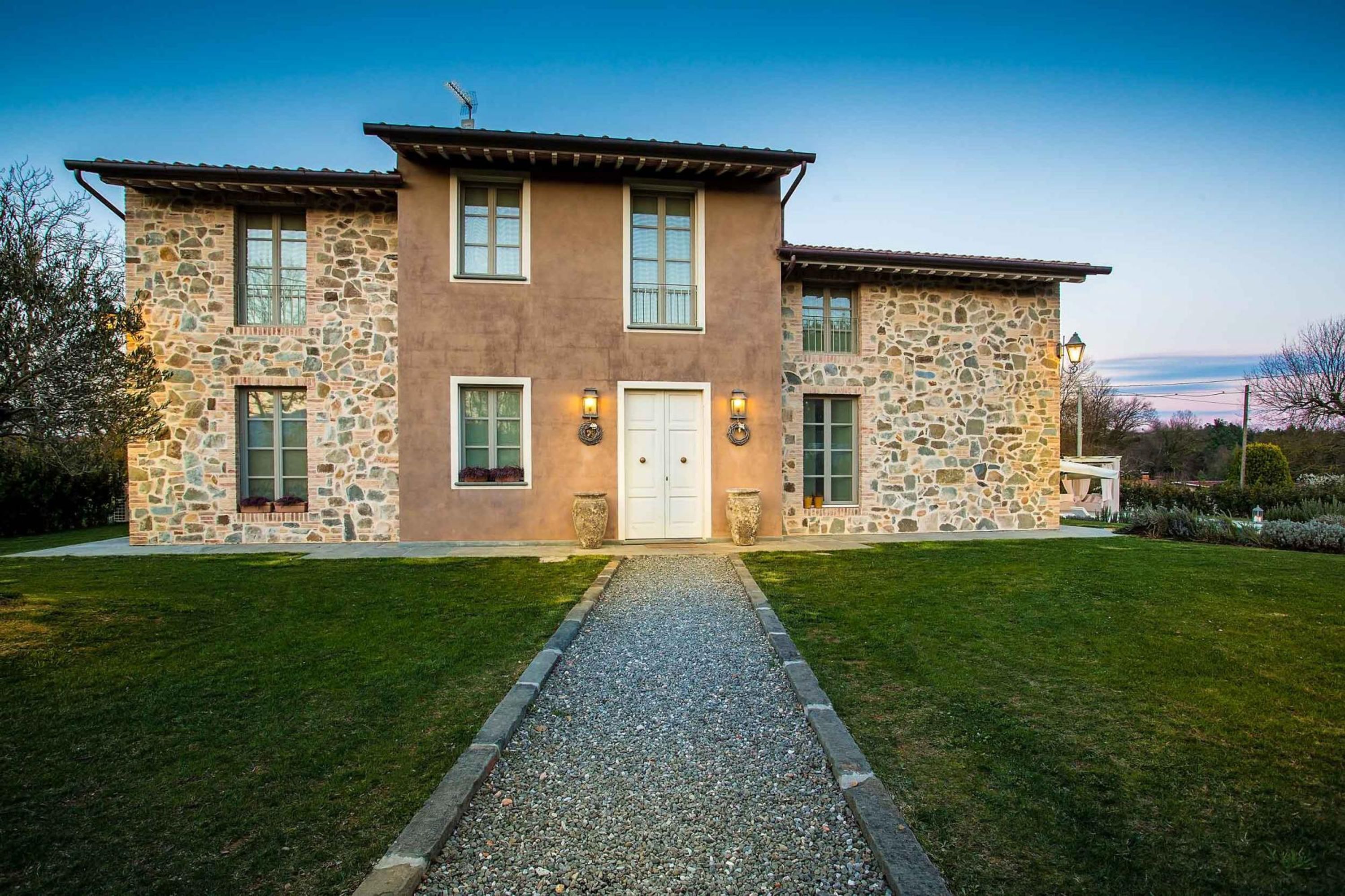 A two-story stone house with a gravel driveway and a well-maintained lawn.