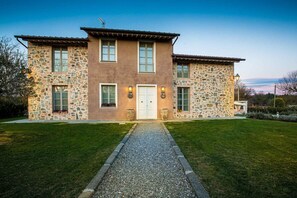 A two-story stone house with a gravel driveway and a well-maintained lawn.