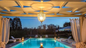 A swimming pool with lounge chairs and candles, under a pergola with curtains. - Villa Otto in Orentano (Castelfranco di Sotto)