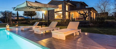 Zona junto a la piscina con sillones de descanso y un área de estar cubierta.