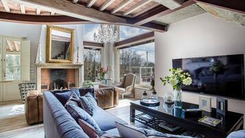 A living room with a fireplace, a large sofa, a television, and a chandelier.