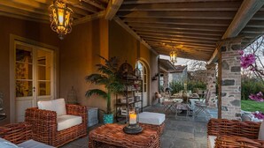 A covered outdoor seating area with wicker furniture, a table set for dining, and a potted plant. - Villa Otto in Orentano (Castelfranco di Sotto)