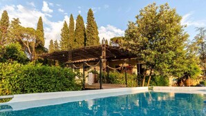 Una piscina con struttura a pergola, immersa nel verde e circondata da alberi alti.