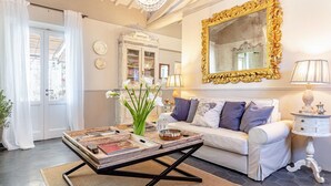 Un soggiorno con un divano bianco, un tavolino da caffè con riviste, uno specchio con cornice dorata e un lampadario.