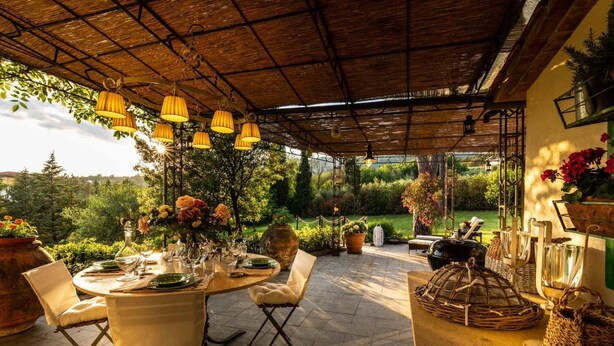 Patio esterno con tavolo rotondo apparecchiato per consumare un pasto, circondato da sedie.