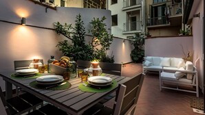 An outdoor dining area with a table set for two, surrounded by greenery and a white sofa. - Villa Paola in Viareggio (Viareggio)