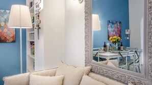A room with a large mirror, a sofa with cushions, a lamp, a bookshelf, and a dining area with a table and chairs. - Villa Paola in Viareggio (Viareggio)