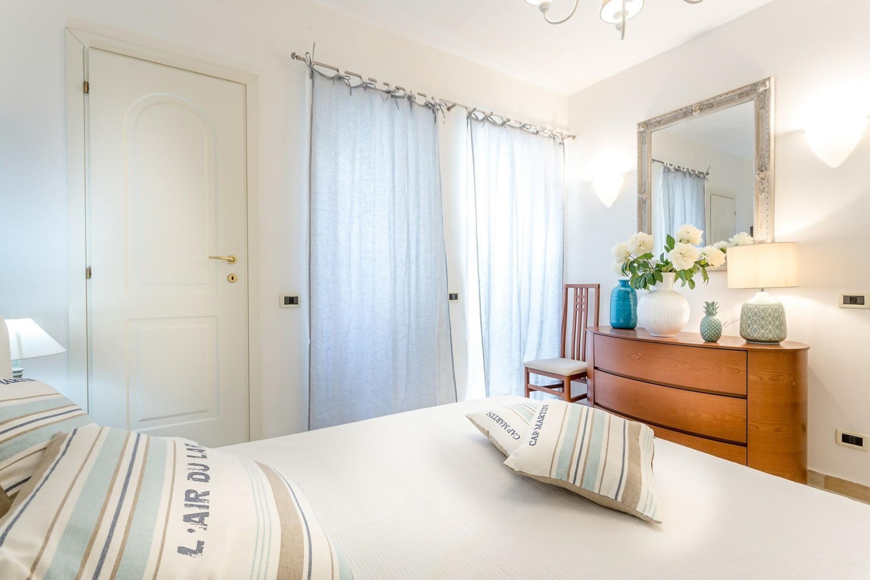 Une chambre d’hôtel avec un lit, une commode en bois, un miroir et une chaise.