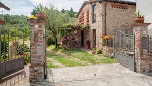 A stone house with a gated entrance, a small garden with flowering plants, and a stone pathway leading to the door. - Villa Pallina in Aquilea (Lucca)
