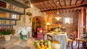 A rustic dining area with stone walls, wooden beams, and a table set with fruits and flowers. - Villa Pallina in Aquilea (Lucca)