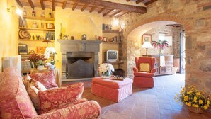 A cozy living room with a fireplace, comfortable seating, and a stone wall. - Villa Pallina in Aquilea (Lucca)