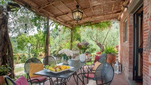 An outdoor patio with a table set for dining, surrounded by chairs and a pergola overhead. - Villa Pallina in Aquilea (Lucca)