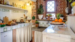 A kitchen with a brick wall, a window, and various kitchen items on the counter. - Rosyabate Cottage in Uzzano (Uzzano)