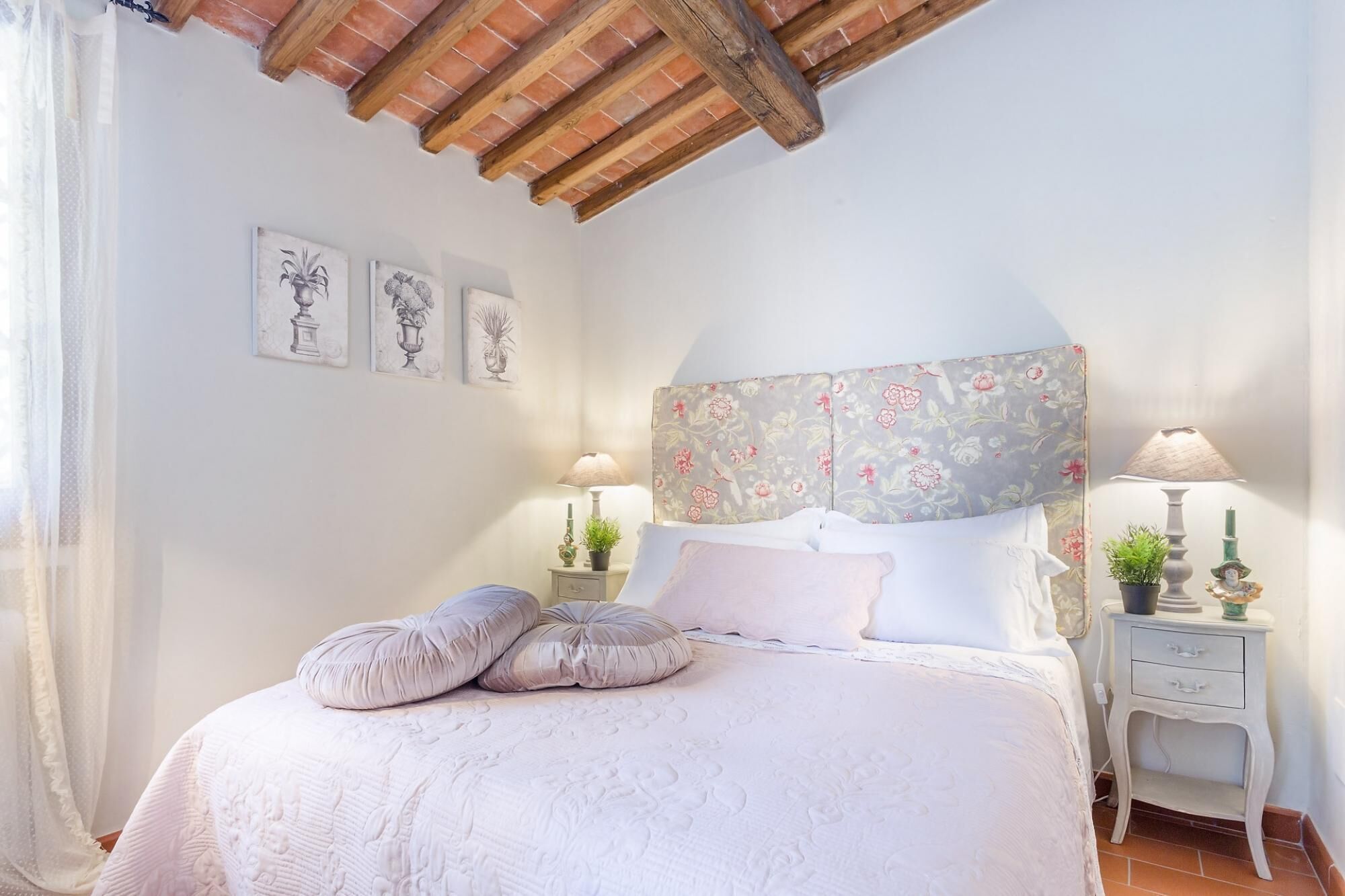 Un dormitorio con una cama, dos mesitas de noche, un cabecero floral y tres cuadros colgados en la pared.