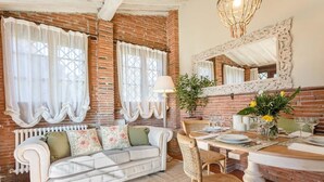 A cozy dining area with a brick wall, white upholstered sofa, wicker chairs, and a table set for two with glasses and a vase of flowers. - Rosyabate Cottage in Uzzano (Uzzano)