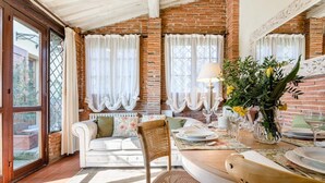 A cozy dining area with a brick wall, white curtains, a white sofa, and a table set for dining. - Rosyabate Cottage in Uzzano (Uzzano)