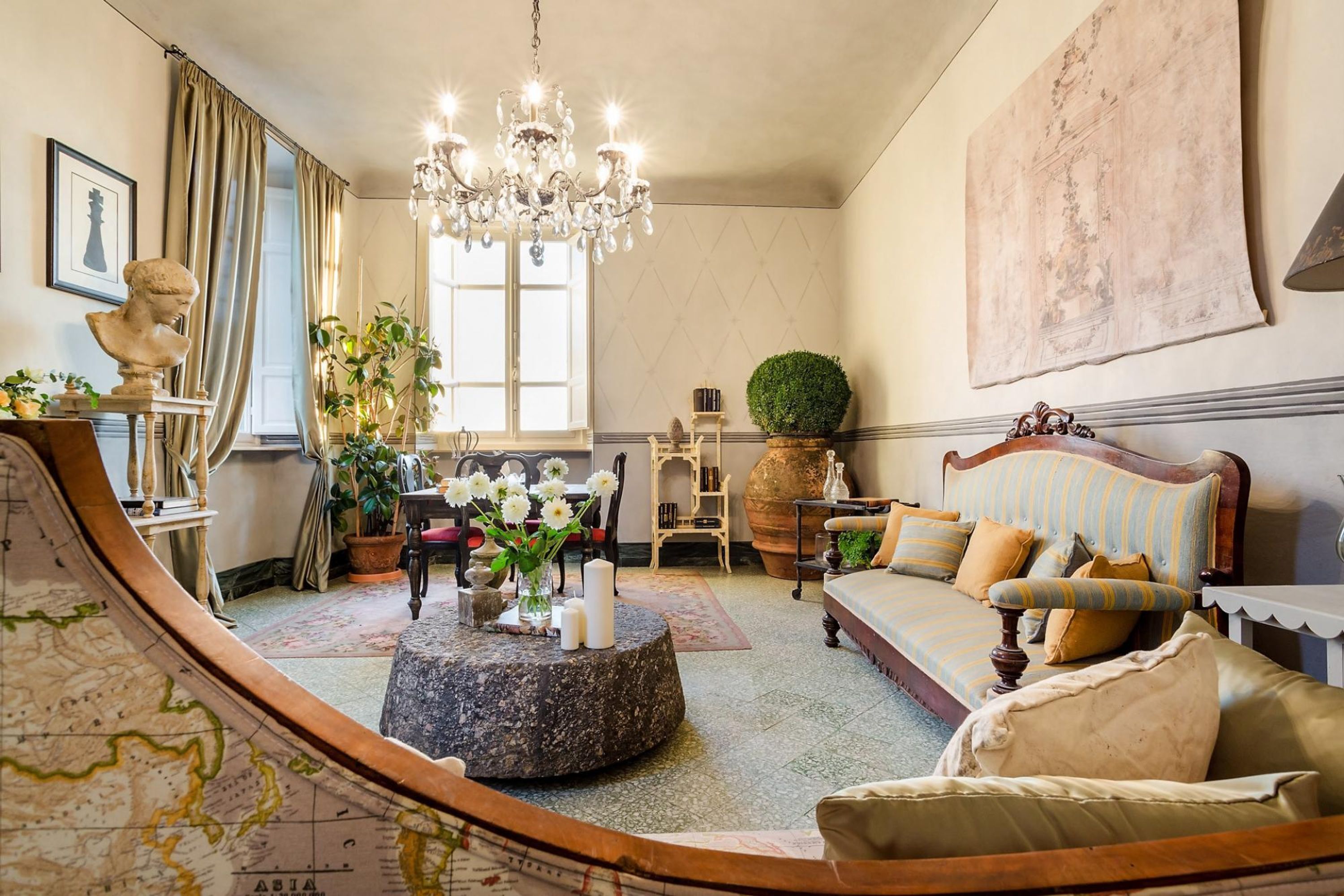 A cozy living room with a round coffee table, a sofa, a chandelier, and a large window.