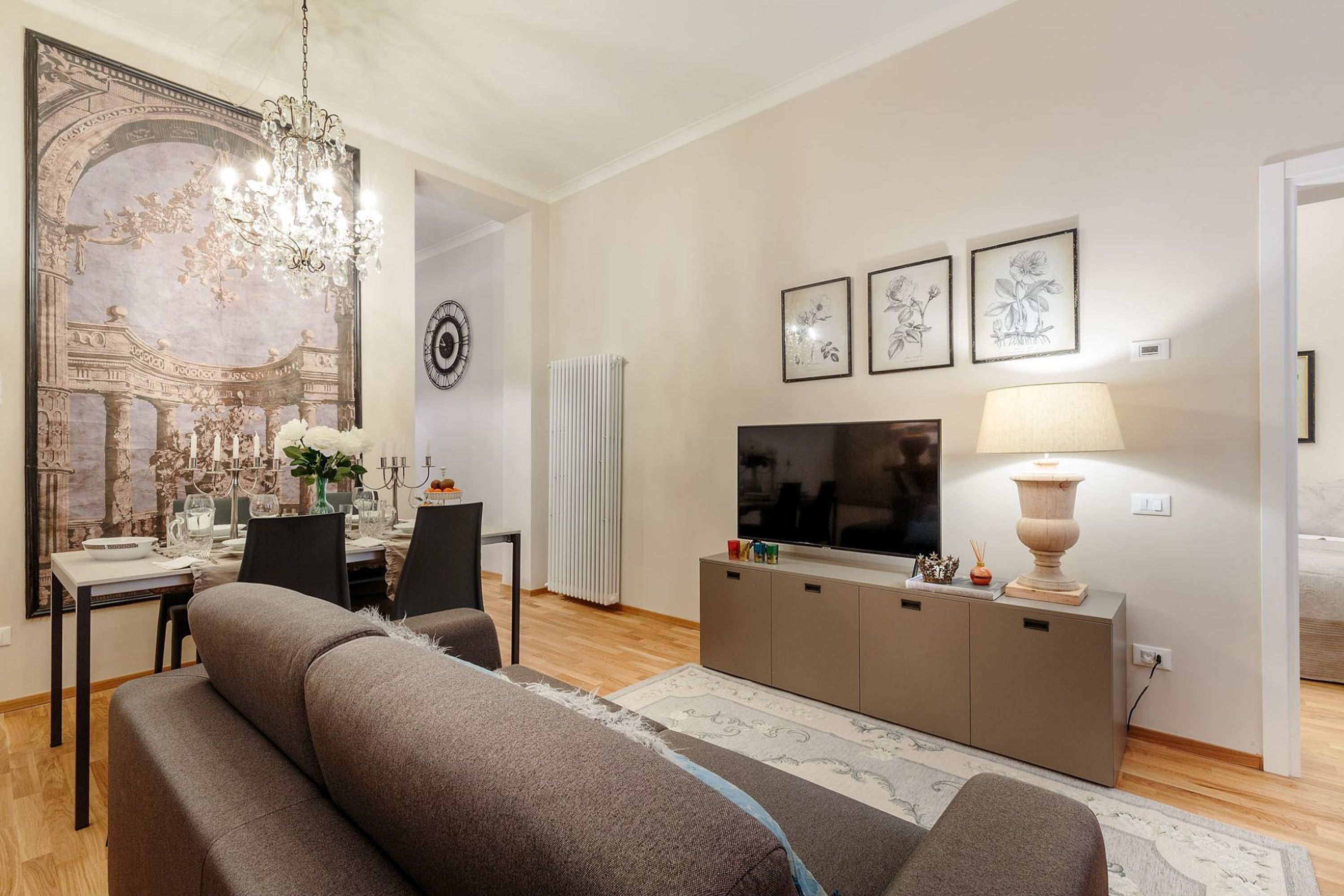 A modern living room with a sofa, a dining table set, a TV, and artwork on the wall.