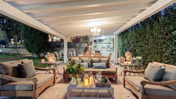 An outdoor patio with wooden furniture, a chandelier, and a stone wall backdrop.