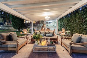 An outdoor patio with wooden furniture, a chandelier, and a stone wall backdrop. - Villa Medea in Maggiano (Lucca)