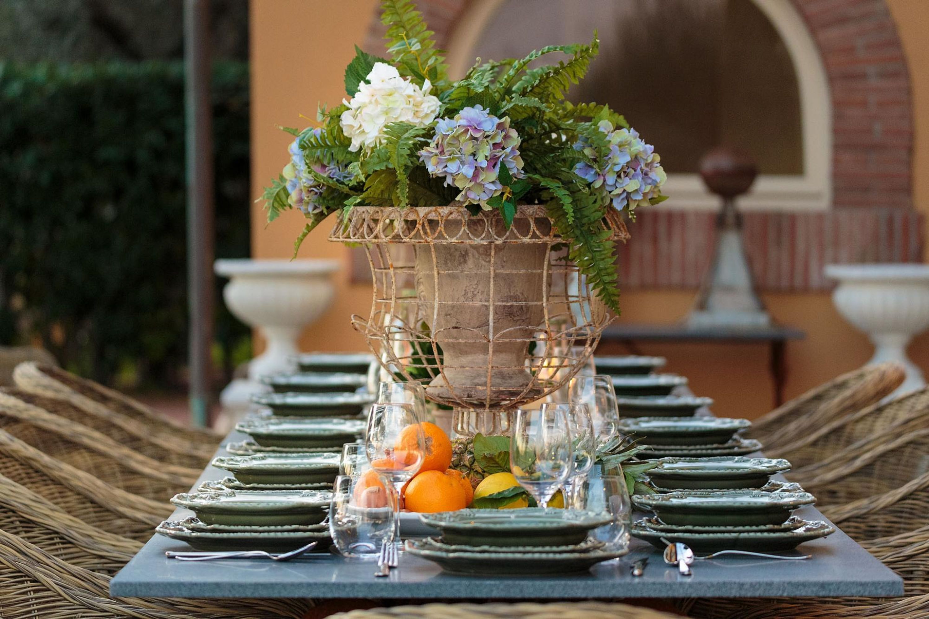 Una mesa servida con platos, vasos y una cesta de frutas.