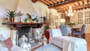 A cozy living room with a fireplace, white furniture, and a dining area with a table set for two. - Villa Viola Residenze Seicento (Capannori)