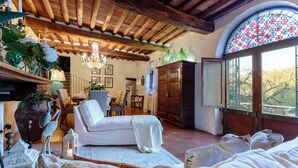 A cozy room with a white sofa, a wooden cabinet, and a large arched window with a stained glass design. - Villa Viola Residenze Seicento (Capannori)