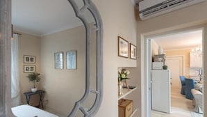 Une pièce avec un grand miroir, une plante en pot, des tableaux encadrés et un réfrigérateur blanc.