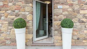 Un bâtiment en pierre avec une porte numérotée, une porte en verre et deux plantes ornementales en pot.
