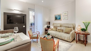 Un salon comprenant un canapé, des fauteuils, un téléviseur et un coin repas avec des assiettes et des verres.