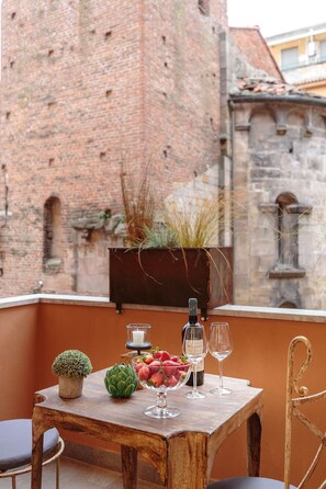 A wooden table with a bottle, glasses, strawberries, and a small plant on a balcony with a brick wall in the background. - The Palace View in Lucca (Lucca)