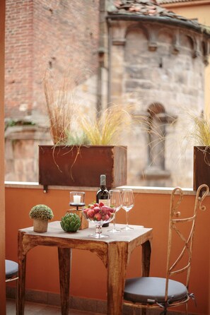 A rustic wooden table with a candle, a bottle, and a glass of red wine, set against a brick wall with potted plants. - The Palace View in Lucca (Lucca)