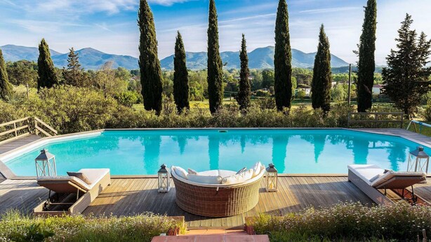 A swimming pool with a wooden deck, lounge chairs, and a wicker chair. - Villa D Amico in Lucca (Lucca)