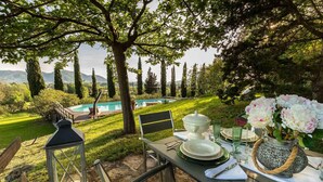An outdoor dining area with a view of a swimming pool, surrounded by trees and a grassy landscape. - Villa D Amico in Lucca (Lucca)