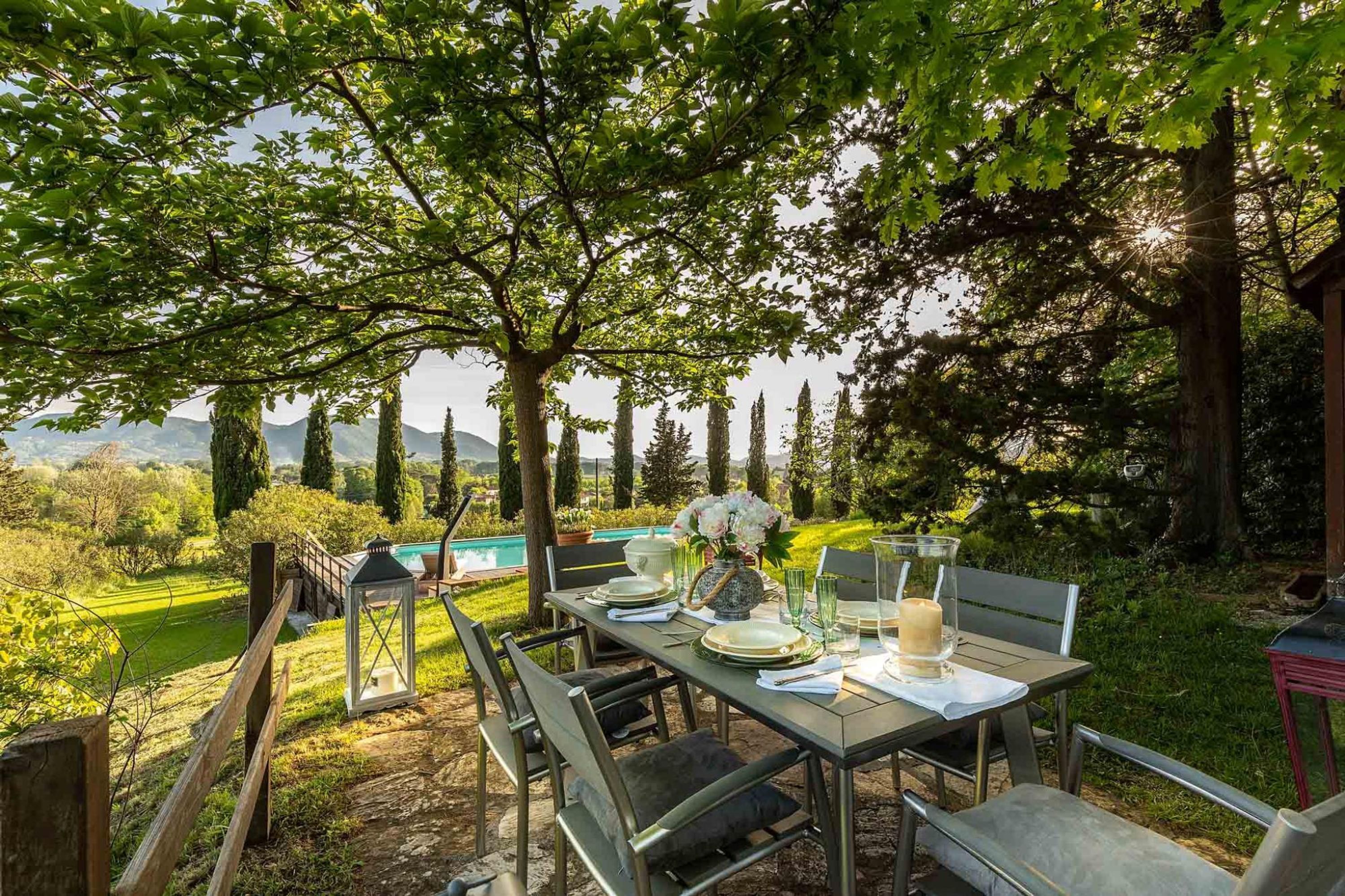An outdoor dining area with a table set for four, surrounded by chairs, in a lush garden with a view of distant mountains.