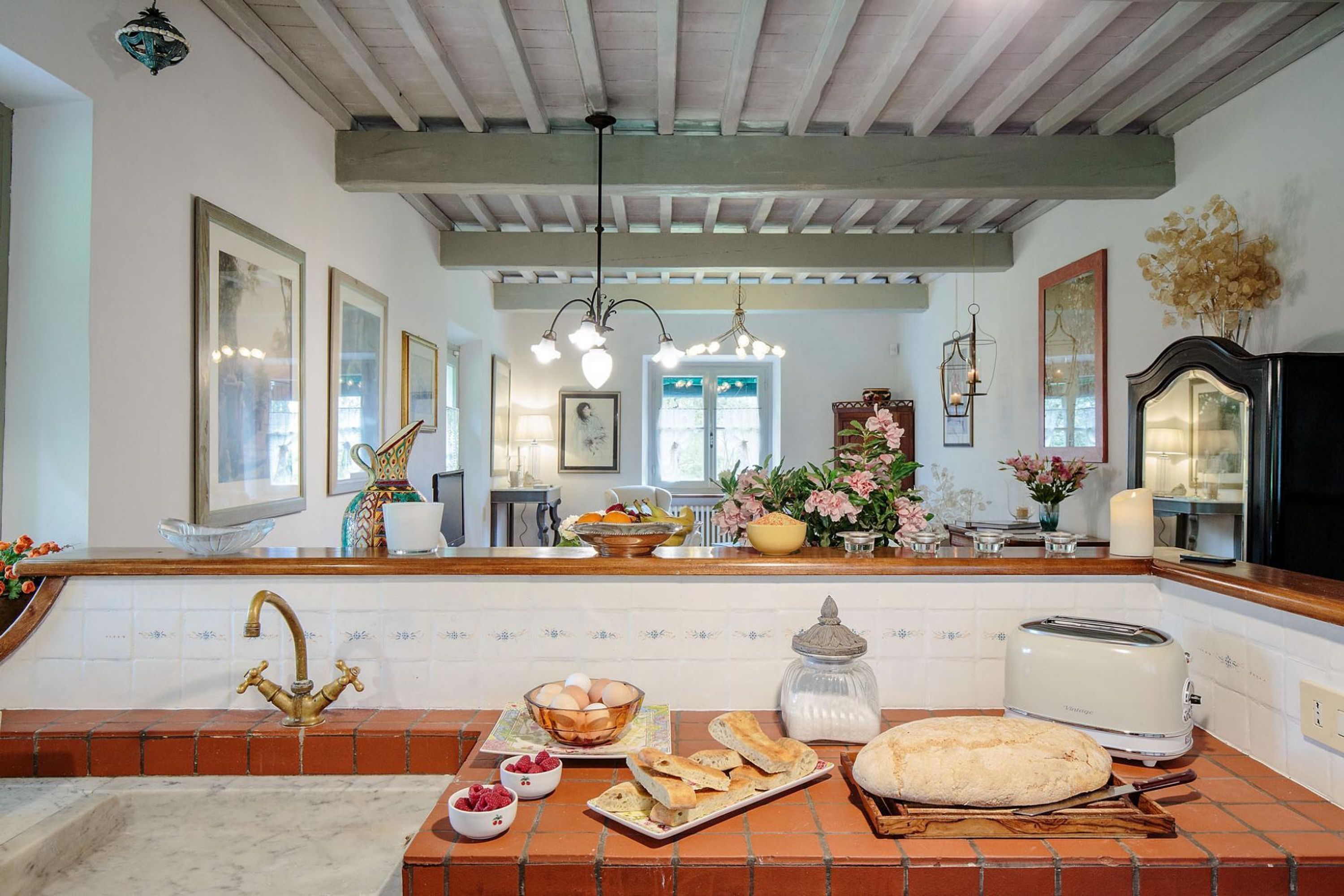 A kitchen with a tiled backsplash, a wooden countertop, a bread loaf, a toaster, and a vase with flowers.