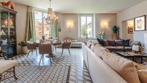 A living room with a sofa, dining table, chairs, and a chandelier. - The Puccini Penthouse (Lucca)