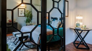 A bedroom with a bed, a bedside table, a chair, a potted plant, and a decorative wall piece. - The Puccini Penthouse (Lucca)