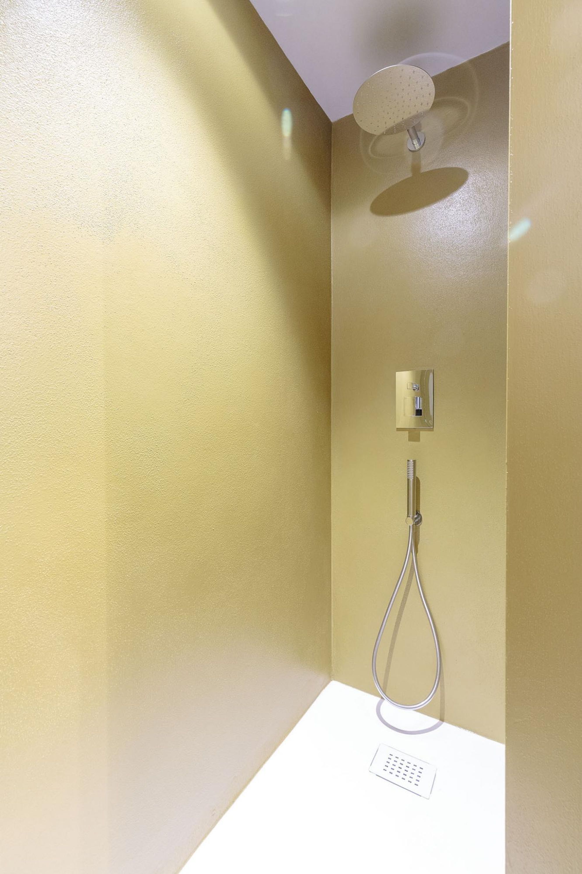 A shower with a handheld showerhead mounted on the wall, a control panel, and a drain.