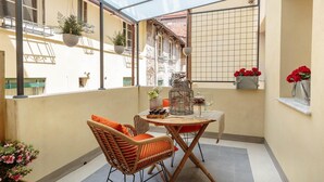A covered balcony with wicker furniture, potted plants, and a tiled floor. - The Puccini Penthouse (Lucca)