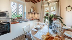 A kitchen with a dining area set for a meal, featuring a microwave, stove, and dining table with chairs. - Villa Pemola in Capannori (Capannori)