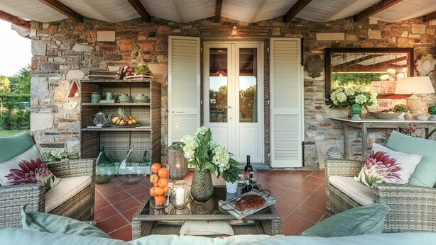 A cozy outdoor seating area with wicker furniture, a stone wall, and a tiled floor. - Villa Pemola in Capannori (Capannori)