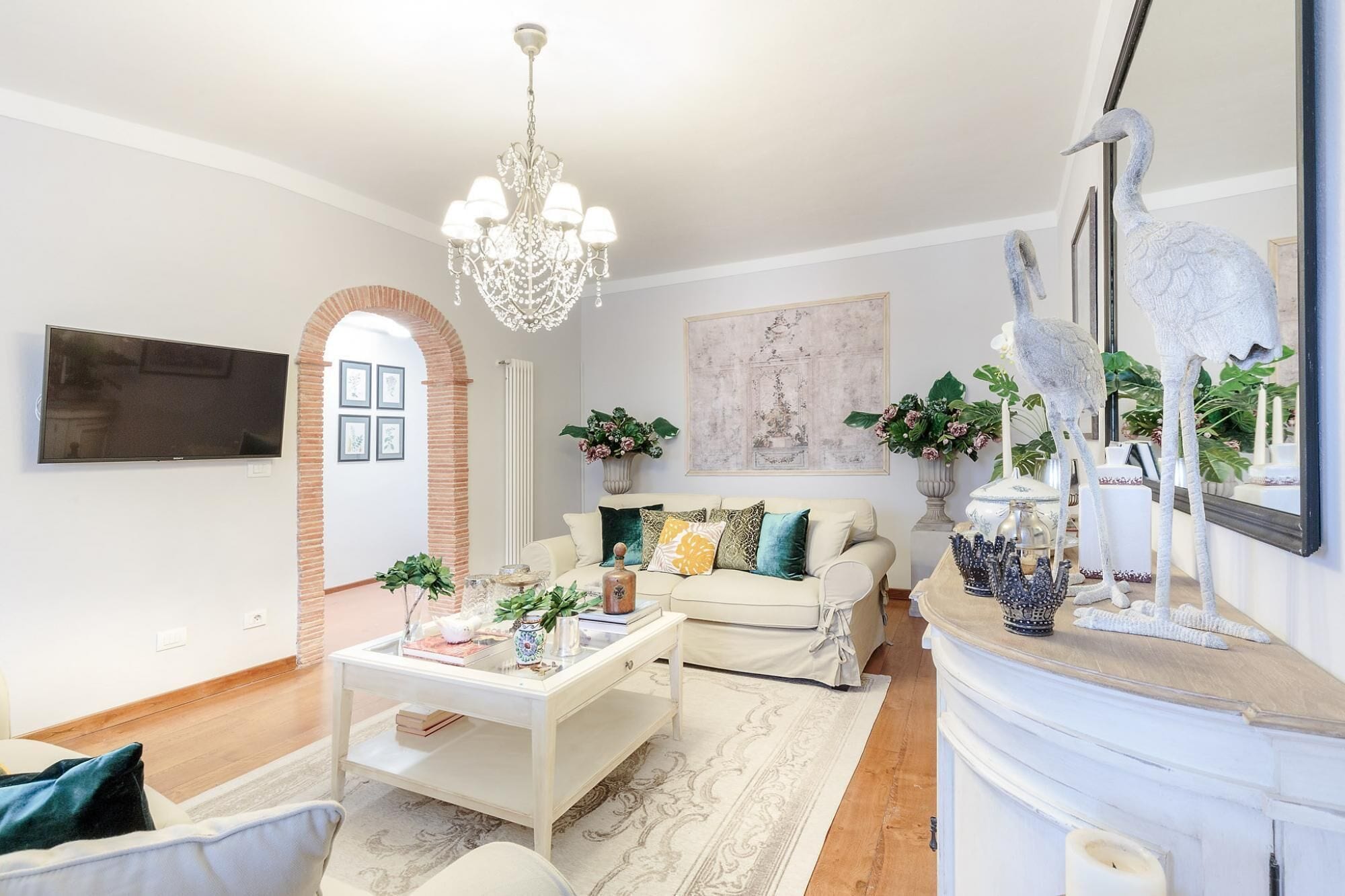 Una sala de estar con un sofá blanco, una mesa de centro, una araña y objetos decorativos.