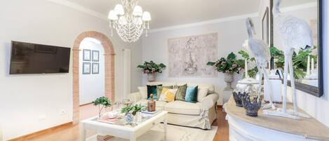 Una sala de estar con un sofá blanco, una mesa de centro, una araña y objetos decorativos.
