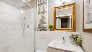 A modern bathroom with a glass-enclosed shower, a white toilet, a sink with a gold-framed mirror, and a vase of flowers. - Casa Santa Croce in Lucca (Lucca)