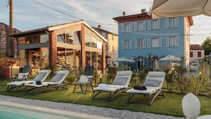 A poolside area with lounge chairs, a pool, and a building with a blue facade and white shutters. - Villa Ricordi in Marlia (Capannori)