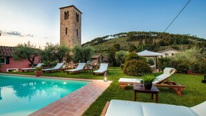 A pool area with lounge chairs and a stone tower in the background. - Villa Matilde in Capannori (Capannori)