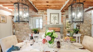 A dining area with a stone wall, wooden ceiling, and hanging lanterns. There is a table set with plates, glasses, and a vase of flowers. - Villa Matilde in Capannori (Capannori)